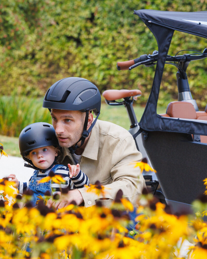 Parent holding a child next to the Lovens Explorer 2 cargo bike with brown leather seats