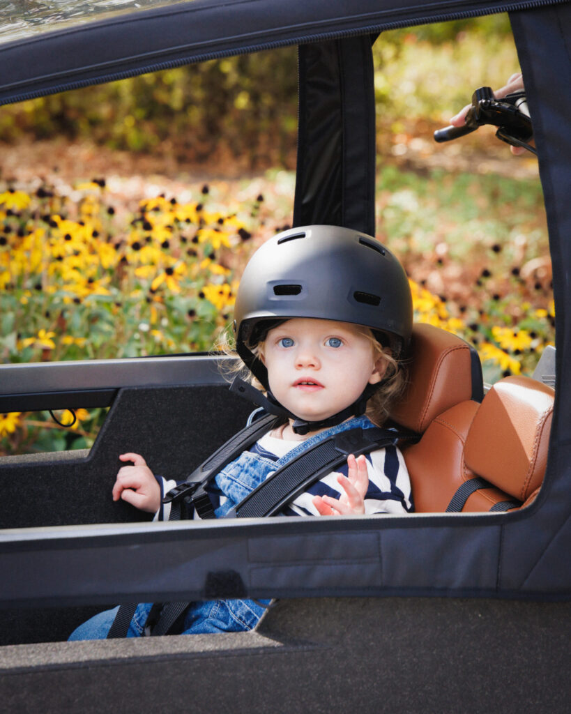 hild wearing a helmet sitting in the Lovens Explorer 2 cargo bike under the rain cover